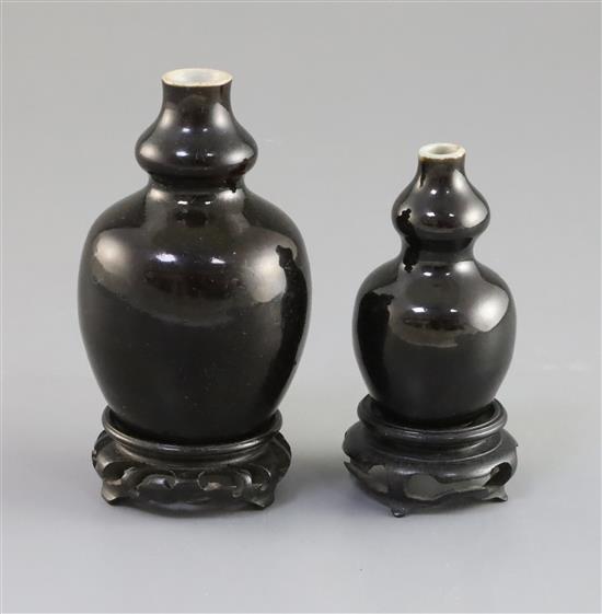 Two Chinese miniature black glazed double gourd vases, 18th century, H. 9.5cm and 7.4cm, tiny rim chip, wood stands